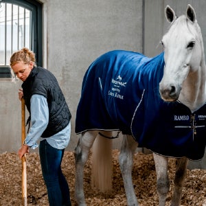 Une femme nettoie l'écurie avec un cheval debout à ses côtés