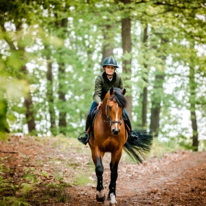 A woman riding a horse through a forest