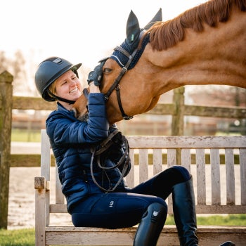 A happy rider sitting on a bench holding their horse's muzzle 