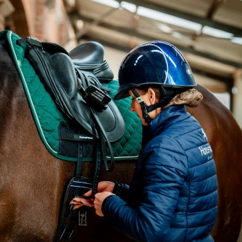 A rider adjusts the saddle on a horse inside a stable